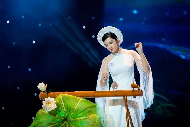 A musician playing the đàn bầu — a one-stringed instrument with a curved rod, the player highly focused