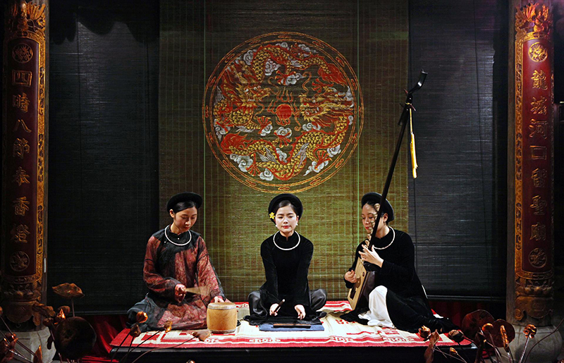 Ca trù artists — the female vocalist (đào hát), the musician playing the đàn đáy, and the spectator beating the praise drum (trống chầu)