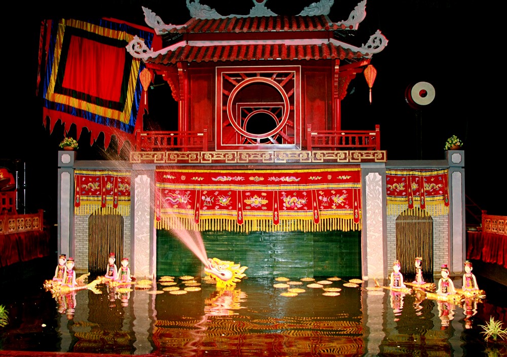 A traditional water puppetry stage — the water surface, the bamboo screen, theatrical lighting — the artisans concealed behind the screen