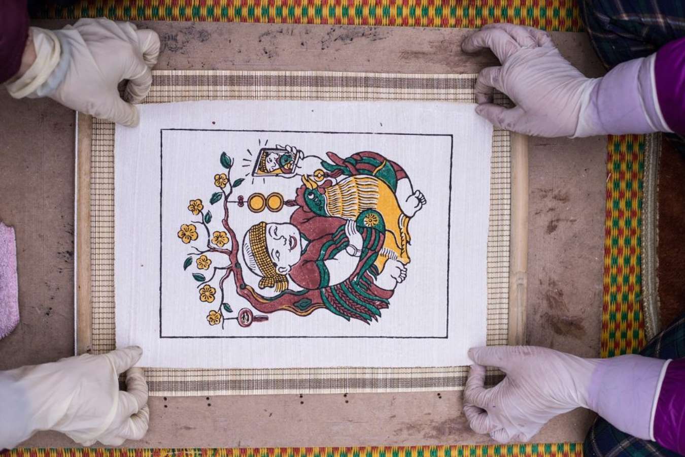 A Đông Hồ printing block — hand-carved wood, sharp details — an artisan in the process of printing