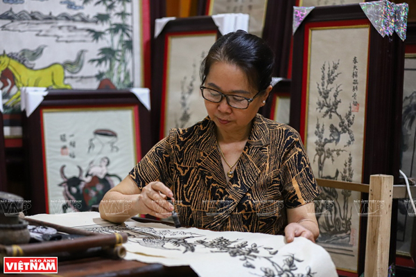 An elderly Đông Hồ master sitting and printing a woodcut — the rustic setting of a traditional craft workshop