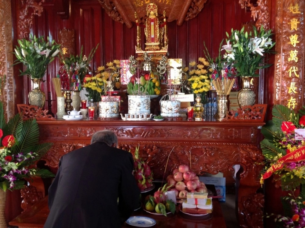 A Vietnamese woman lighting incense with deep reverence before the ancestral altar — a deeply private moment