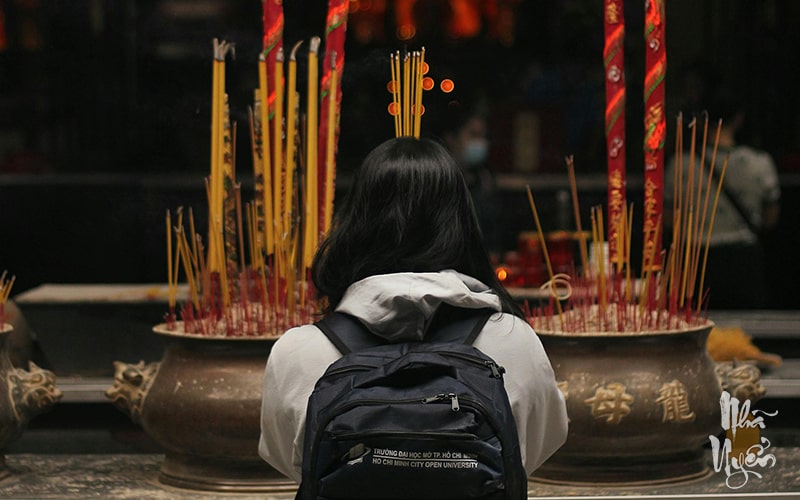 A person's hands lighting incense — white smoke drifting upward — the flickering light of candles