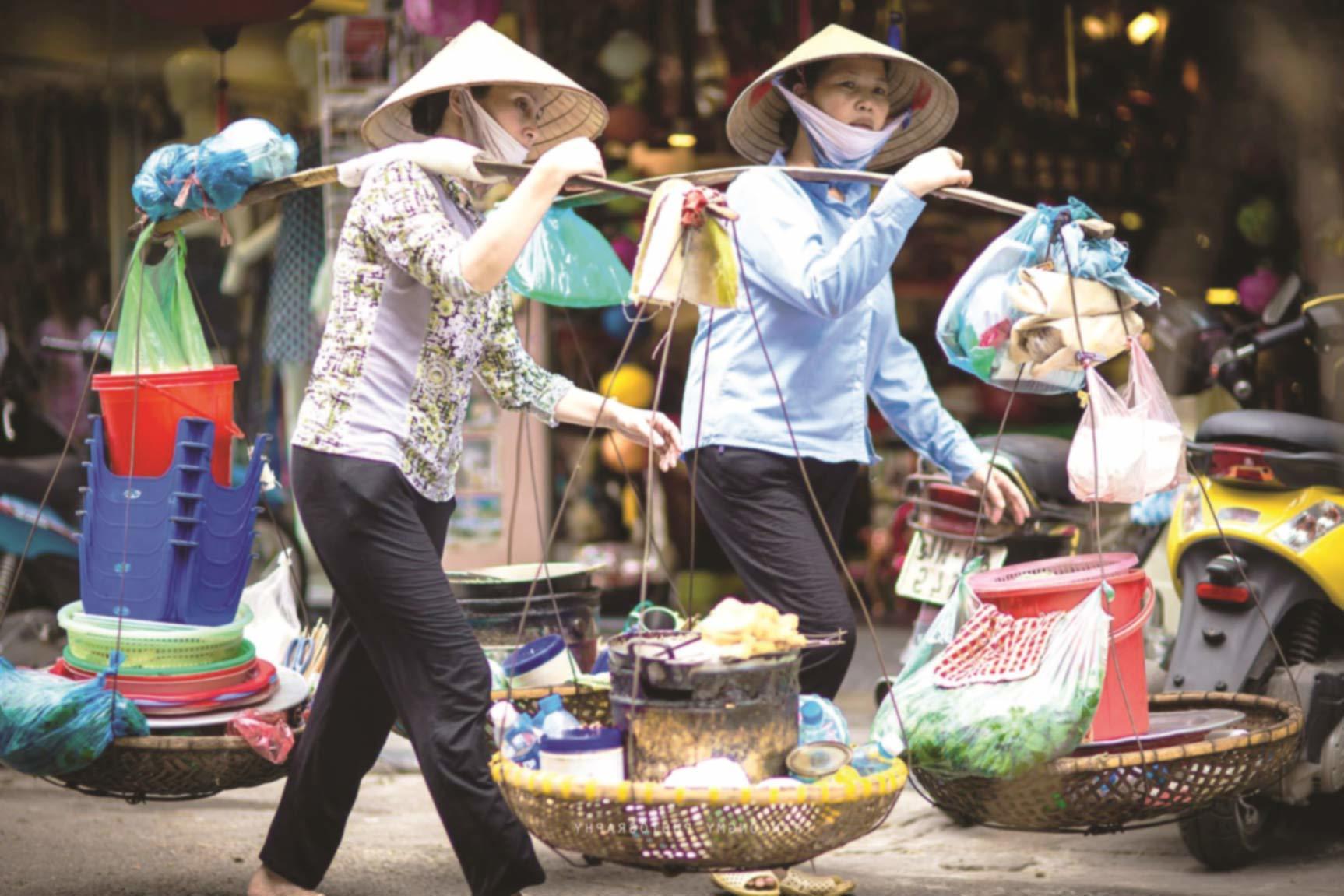 A Vietnamese person calling a vendor "cô" or "chú" — a bright market scene, warm interaction