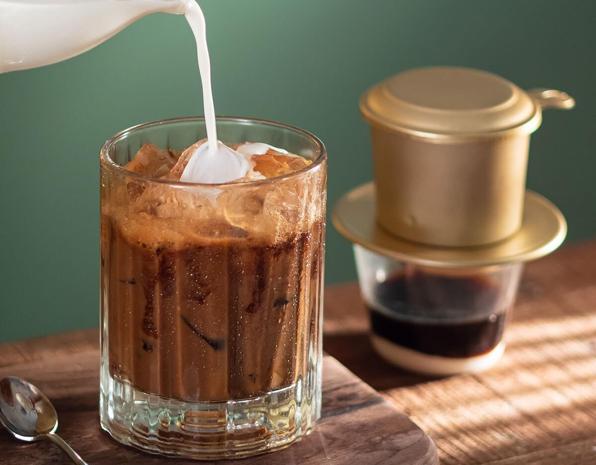 A glass of Vietnamese iced milk coffee — dark amber liquid, stark white ice, and a thick layer of yellow condensed milk at the bottom
