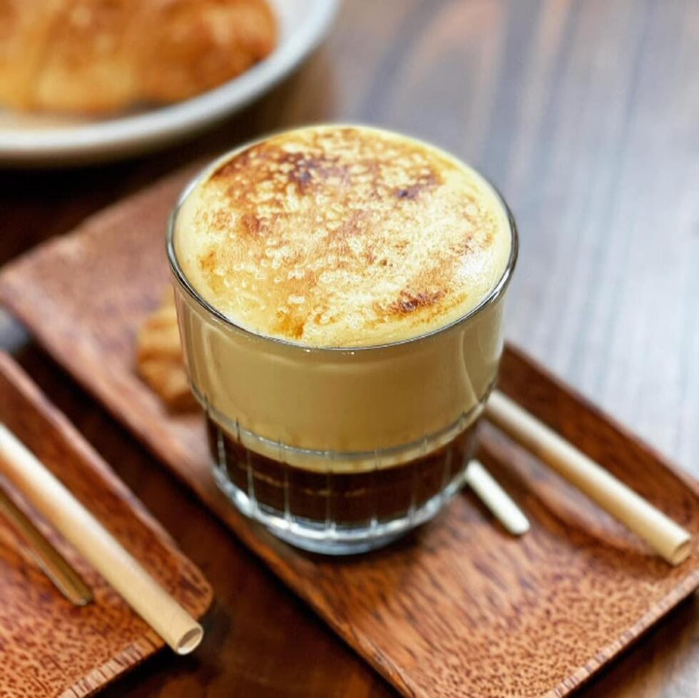 A cup of Hanoi egg coffee — a thick, golden layer of whipped egg cream resting atop dark black coffee