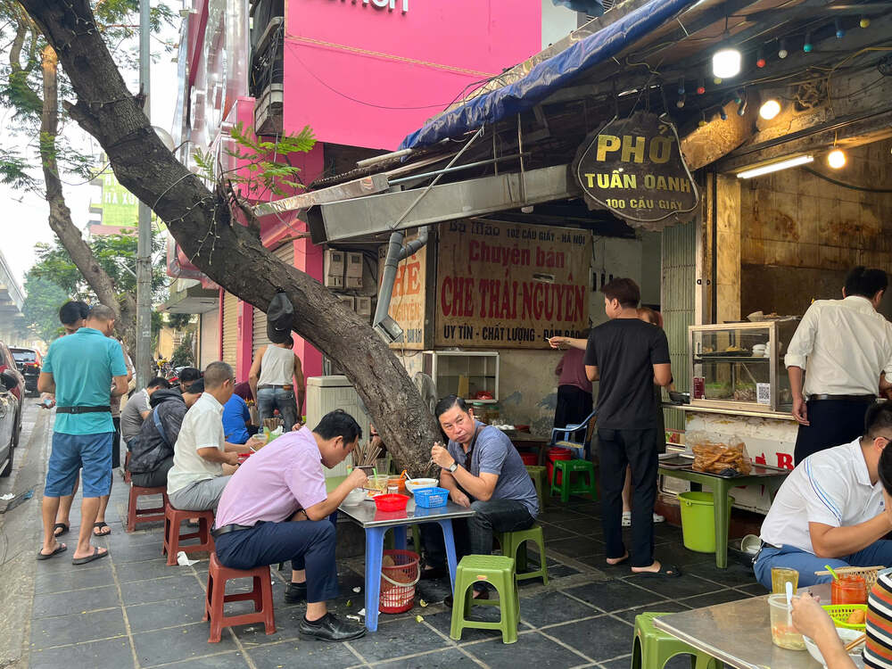 A sidewalk Pho stall that sells absolutely nothing but Pho — the owner stands holding a bowl next to a massive cauldron of boiling broth