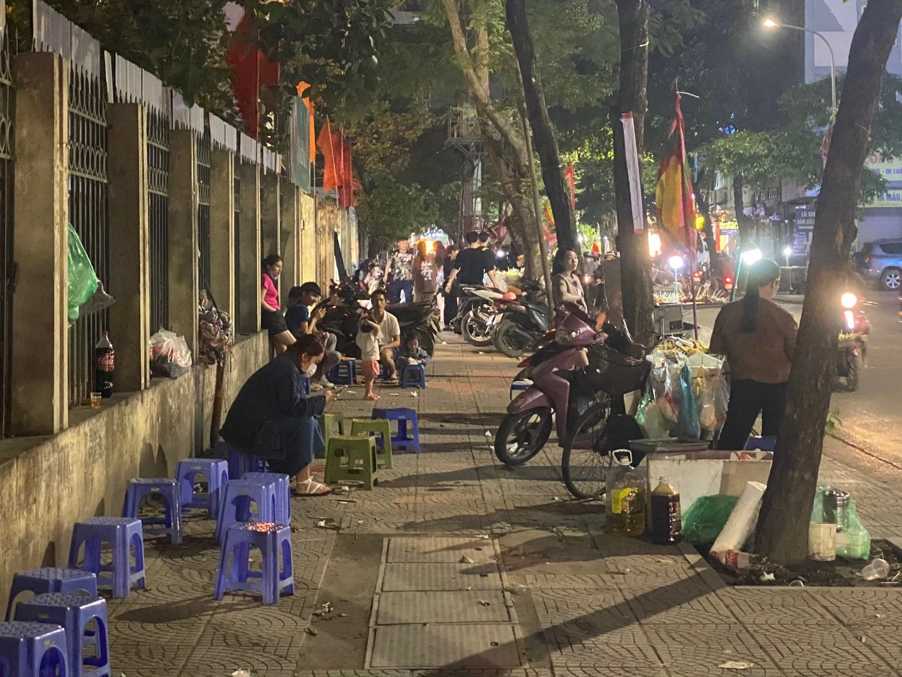 An evening sidewalk corner in Hanoi — people of all ages sitting and eating together under the warm glow of streetlamps