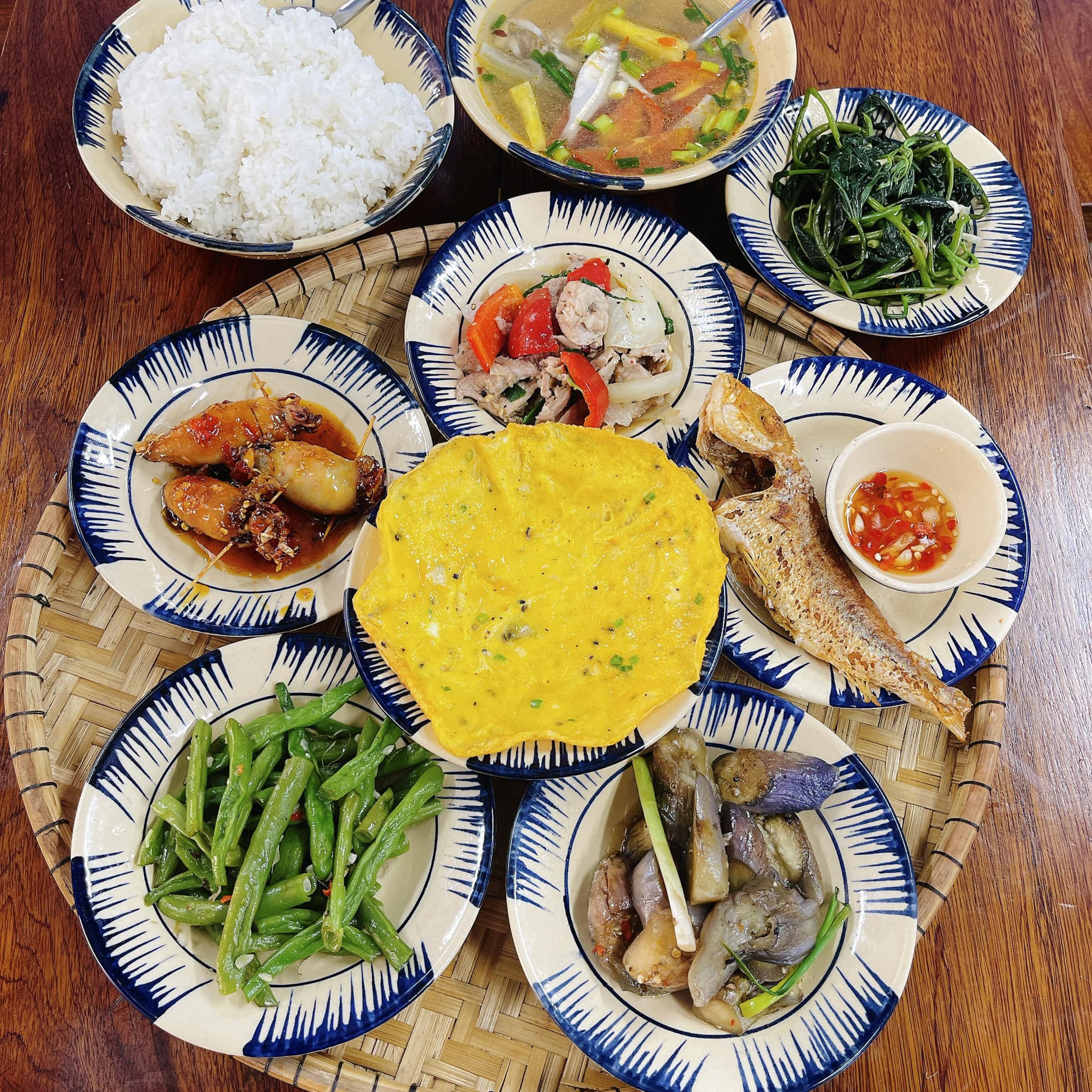 A Hue family meal — numerous tiny, diverse dishes, vibrant red and orange chili tones, a regal atmosphere