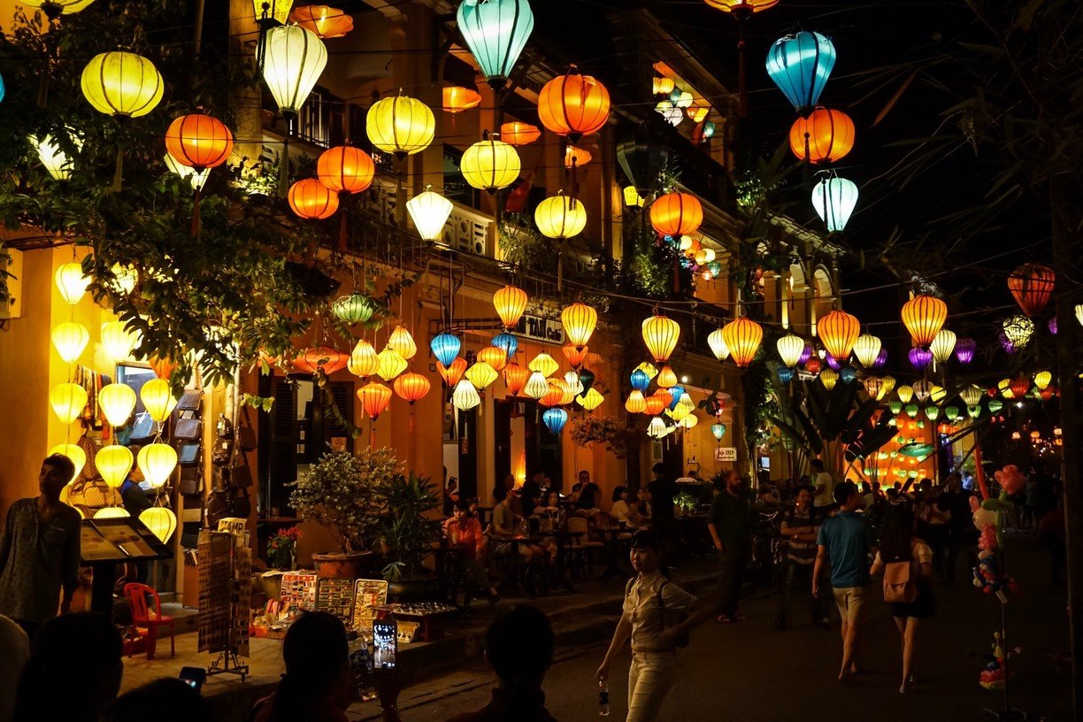 The lantern-lit streets of Hoi An at night — pink and yellow illumination reflecting off ancient architecture