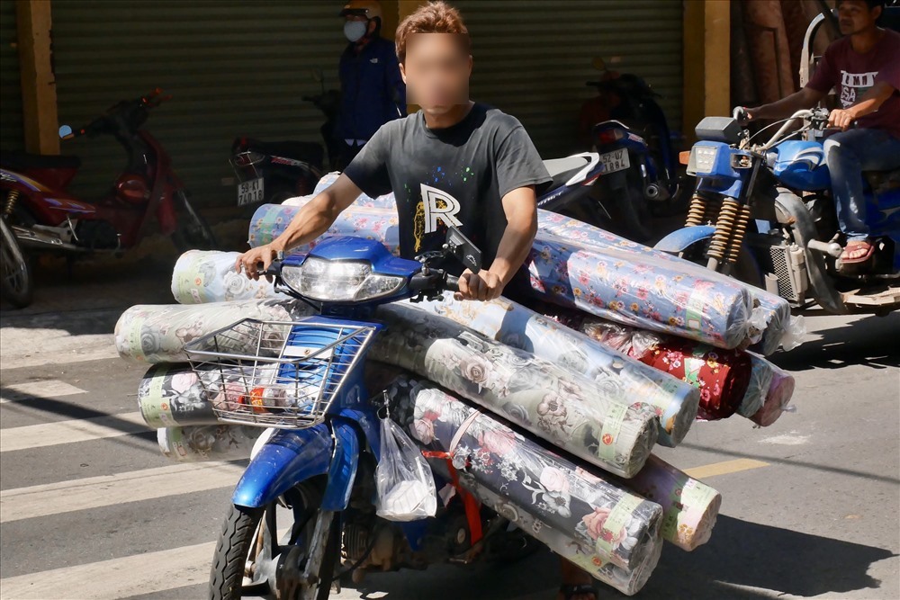 A delivery rider with a completely overloaded motorbike — boxes, bags, and an entire small cabinet strapped to the back